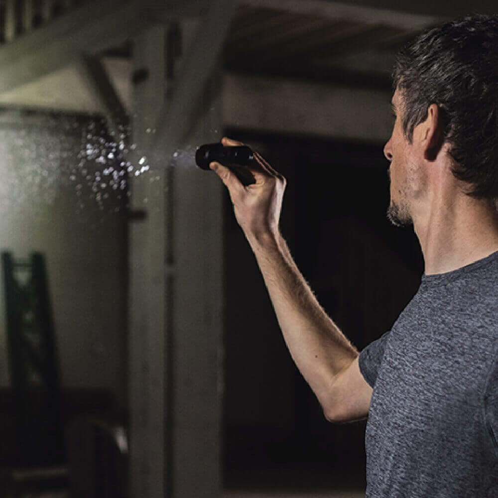 Coast XP11R LED Torch  - Person using a handheld device to spray water on a wall in a dimly lit room.