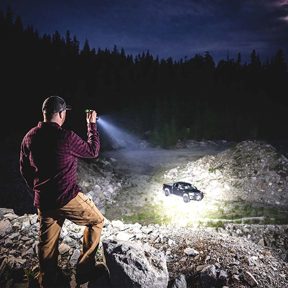 Coast XP40R LED Torch - Person using a flashlight to illuminate a vehicle on a rocky terrain at night.