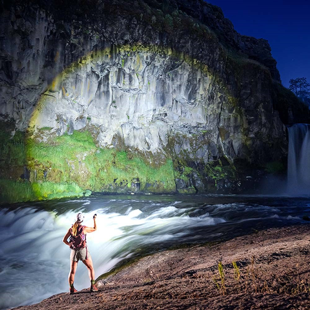 Coast XP80R LED Torch - Person standing near a waterfall with a backpack at night using ab amazing torch