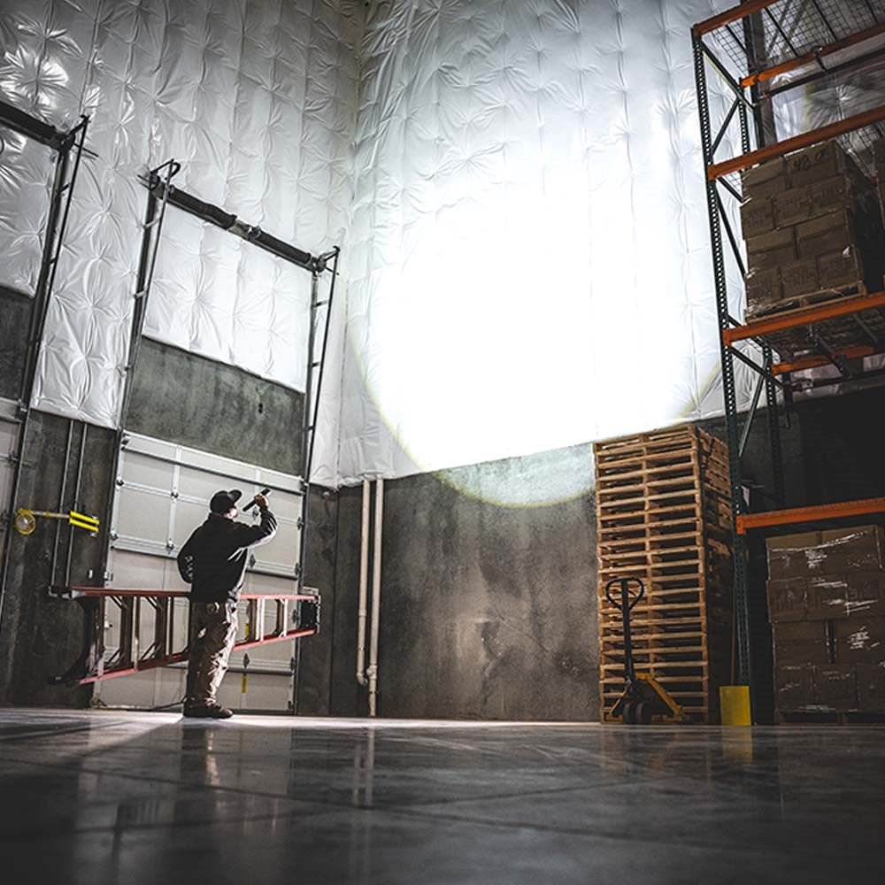 Coast XP80R LED Torch - Person working in a large warehouse with high ceilings and industrial equipment.