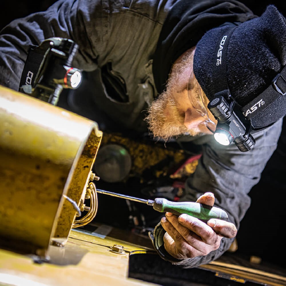 Coast XPH34R LED Headlight - Person working on a mechanical object with a flashlight and tool