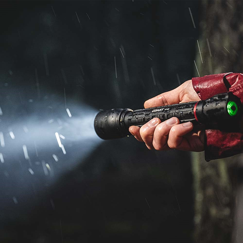 Coast XP14R  Flashlight - Hand holding a flashlight emitting light in a dark setting